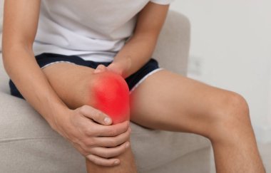 Evdeki koltukta dizinde ağrıdan muzdarip bir adam, yakın plan.