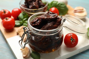 Lezzetli güneşte kurutulmuş domatesler, taze sebzeler, fesleğen ve sarımsak mavi ahşap masada, yakın plan.