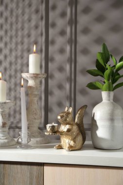 Zarif şamdanlar, yanan mumlar, vazoda dallar ve gri duvarın yanındaki şifoniyerde diğer dekorlar.