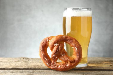 Lezzetli kraker ve bir bardak bira ahşap masada, gri arka planda, yakın planda.