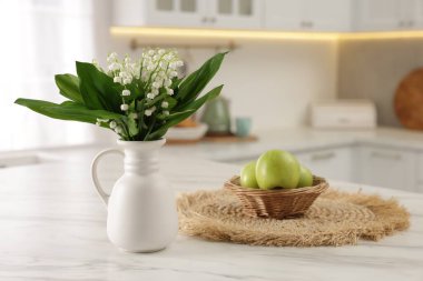 Vazodaki güzel zambak buketi ve mutfaktaki beyaz mermer masada elmalar.