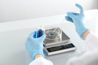 Laboratuvardaki beyaz ayna masasında numune ve terazilerle çalışan bilim adamı.