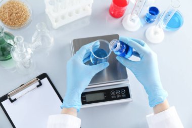 Beyaz ayna masasında numune ve terazilerle çalışan bilim adamı.