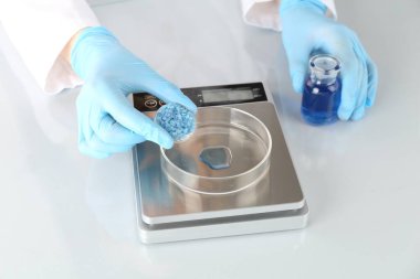 Laboratuvardaki beyaz ayna masasında numune ve terazilerle çalışan bilim adamı.