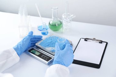 Bilim adamı beyaz masadaki terazide numune tartıyor, yakın plan.