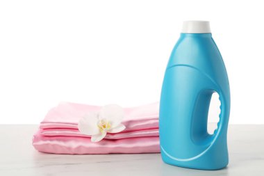 Bir şişe yumuşatıcı, üst üste yığılmış giysiler ve çiçek beyaz arka plana karşı mermer masa