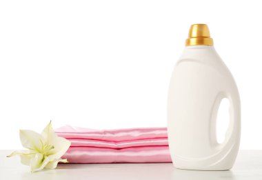 Bir şişe yumuşatıcı, üst üste yığılmış giysiler ve çiçek beyaz arka plana karşı mermer masa