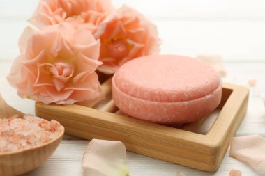 Sabun çubuğu, deniz tuzu ve beyaz ahşap masada güzel çiçekler, yakın plan.