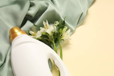 Bir şişe yumuşatıcı, çiçekler ve bej arka planda yeşil kumaş. Metin için boşluk