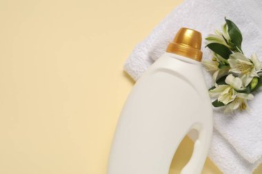 Bir şişe yumuşatıcı, çiçekler ve bej arka planda terry havlular, düz yatak. Metin için boşluk