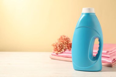 Bir şişe yumuşatıcı, temiz kıyafetler ve karanfil çiçekleri açık sarı arka planda beyaz ahşap masa üzerinde. Metin için boşluk