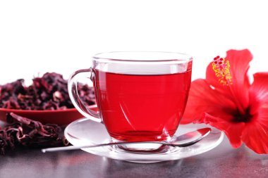 Lezzetli bardakta amber çayı, kuru roselle sepals ve beyaz arka planda gri desenli masada güzel bir çiçek.