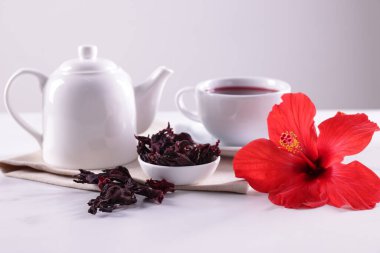 Lezzetli amber çayı, kuru roselle sepals ve güzel çiçek beyaz masada gri arka planda, yakın planda.