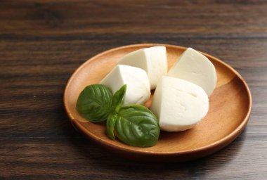 Ahşap masada lezzetli mozzarella peyniri ve fesleğen parçaları, yakın plan.
