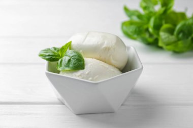 Lezzetli mozzarella peyniri ve fesleğen parçaları beyaz ahşap masada, yakın plan.