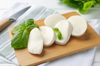 Lezzetli mozzarella peyniri ve fesleğen yaprakları beyaz ahşap masada, yakın plan.