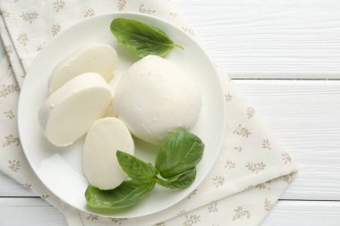 Beyaz ahşap masa üzerinde lezzetli mozzarella peyniri ve fesleğen parçaları.