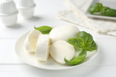 Lezzetli mozzarella peyniri ve fesleğen parçaları beyaz ahşap masada, yakın plan.