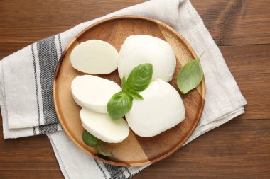 Lezzetli mozzarella peyniri ve fesleğen yaprakları ahşap masanın üstünde.