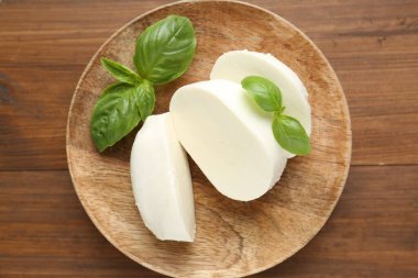Lezzetli mozzarella peyniri ve fesleğen yaprakları ahşap masanın üstünde.