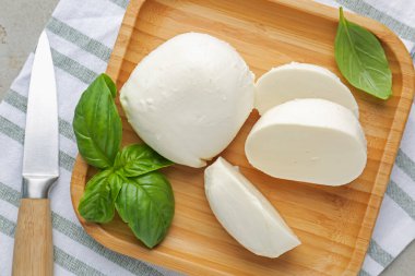 Lezzetli mozzarella peyniri parçaları, fesleğen yaprakları ve bıçak gri masada, üst manzara