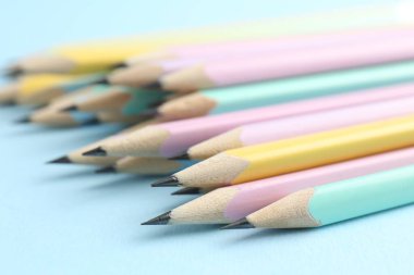 Many graphite pencils on light blue background, closeup