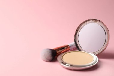 Aynalı açık yüz pudrası ve pembe arka planda fırça, yakın plan. Metin için boşluk