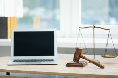 Dizüstü bilgisayar, yargıç tokmağı ve terazileri ofisteki ahşap masada.