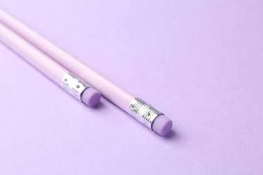 Menekşe arka planında silgi olan iki grafit kalem, yakın plan. Metin için boşluk