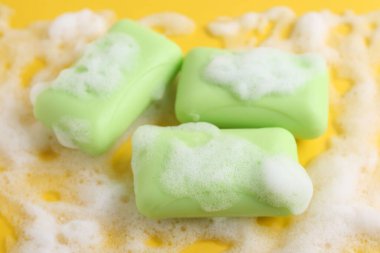 Sarı arka planda köpüklü sabun çubukları, yakın plan.