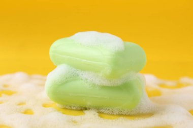 Sarı arka planda köpüklü sabun çubukları, yakın plan.