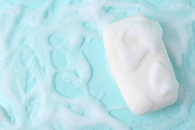 Açık mavi arka planda köpüklü sabun çubuğu, üst manzara. Metin için boşluk