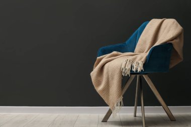 Gri duvarın yanında bej yün battaniyeli rahat koltuk, metin için yer