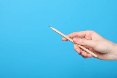 Açık mavi arka planda grafit kalemi olan kadın, yakın plan. Metin için boşluk