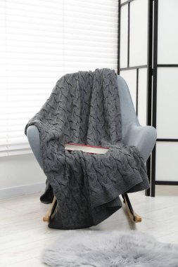 Rahat koltuk, gri yün battaniye ve kapalı bir kitap.