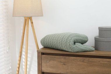 Yeşil yün battaniye, ahşap sandıktaki kutular ve beyaz duvarın yanındaki lamba, yakın plan.