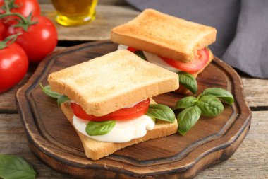 Mozarella peynirli, domatesli ve ahşap masadaki fesleğenli lezzetli sandviçler.