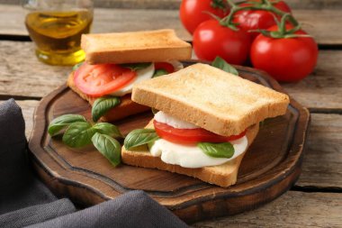 Mozarella peynirli, domatesli ve ahşap masadaki fesleğenli lezzetli sandviçler.