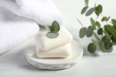 Sabun çubukları, havlular ve okaliptüs dalları beyaz mermer masa üzerinde, yakın plan.