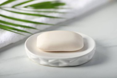 Sabun çubuğu, havlu ve palmiye yaprağı beyaz mermer masada, yakın plan.