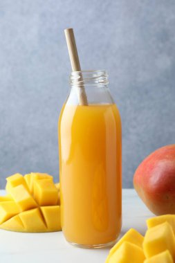 Cam şişede lezzetli mango suyu ve beyaz masada taze meyve.