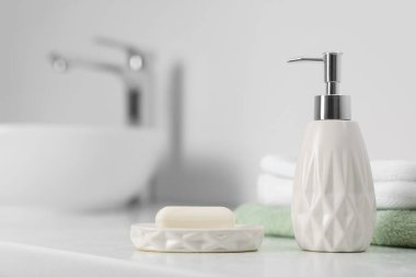 Sabun barı, kozmetik ürünleri şişesi ve banyoda beyaz tezgahta havlular.