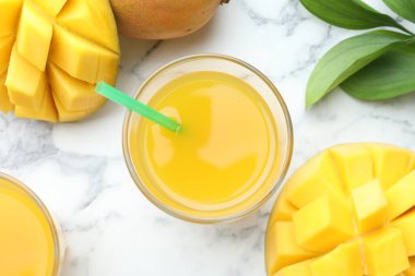Lezzetli mango suyu bardakta, taze meyve ve yeşil yapraklar beyaz mermer masada, düz yerde
