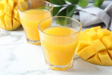 Bardakta lezzetli mango suyu, taze meyve ve yeşil yapraklar beyaz mermer masada, yakın plan.