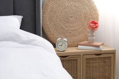 Yatağın yanında çalar saati, dekorasyonu ve kitapları olan bir komodin.