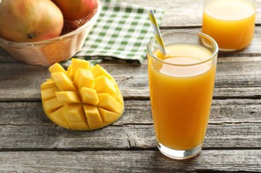 Bardakta lezzetli mango suyu ve ahşap masada taze meyve, yakın plan.