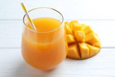 Bardakta lezzetli mango suyu ve beyaz ahşap masada taze meyve, yakın plan.