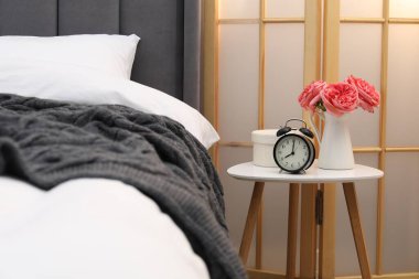 Çalar saati olan yan masa ve yatağın yanındaki dekor.