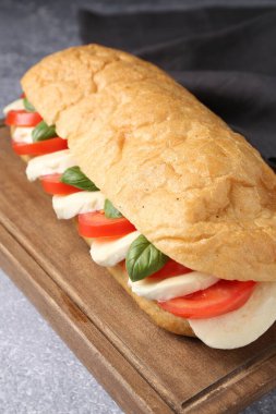 Mozarella peynirli, domatesli ve fesleğenli lezzetli sandviç. Gri desenli masa, yakın plan.