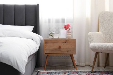 Yatağın yanında kahve, çiçek ve çalar saat olan komodinin yanında.